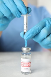 Photo of Doctor filling syringe with coronavirus vaccine at table in laboratory, closeup