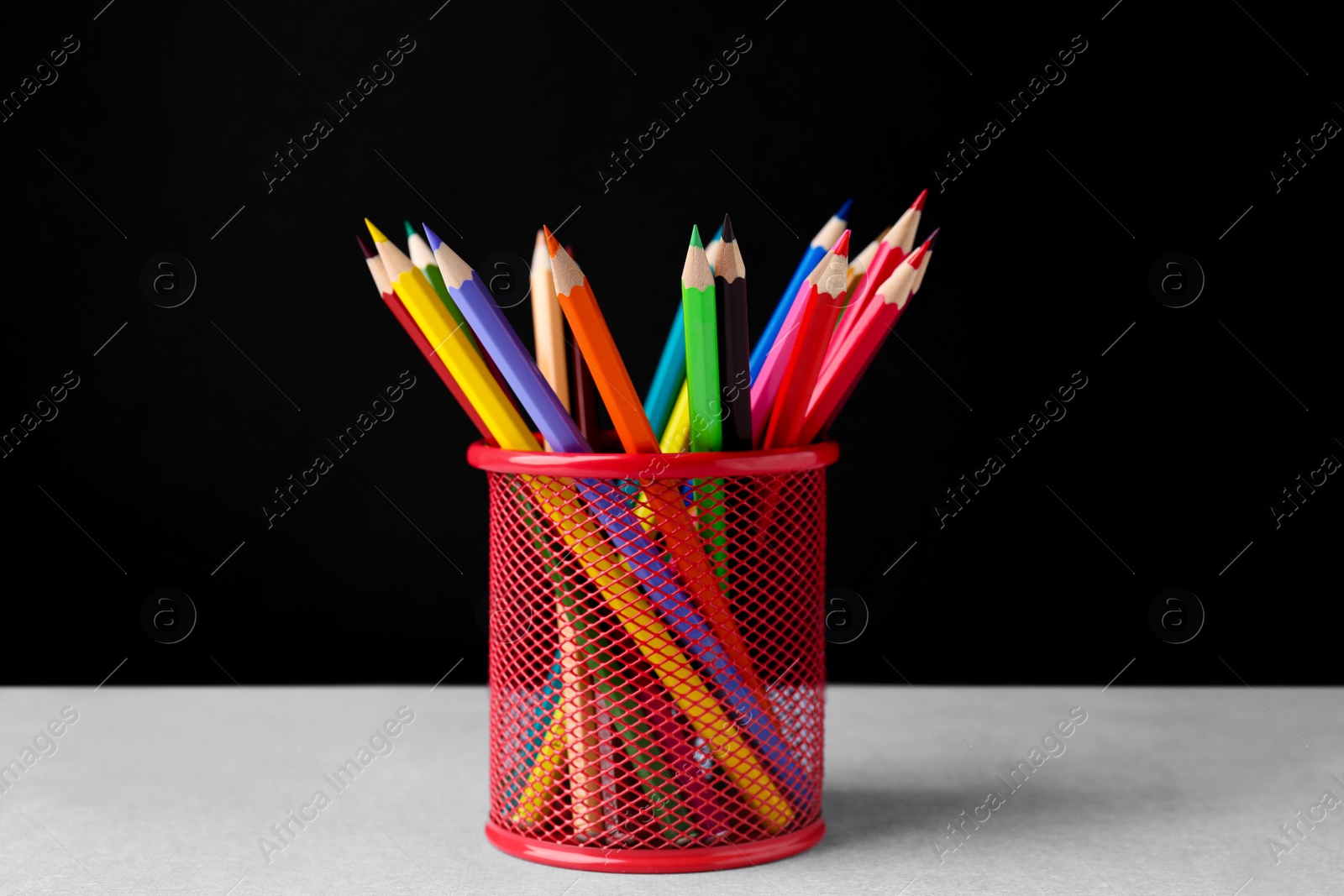 Photo of Many colorful pencils in holder on light table against black background