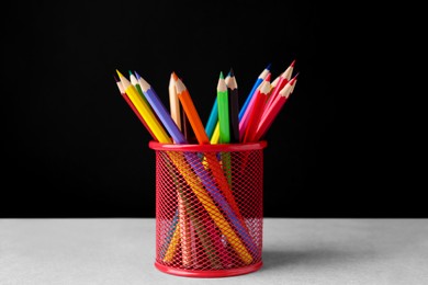 Many colorful pencils in holder on light table against black background