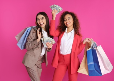 Young women with money and shopping bags on color background