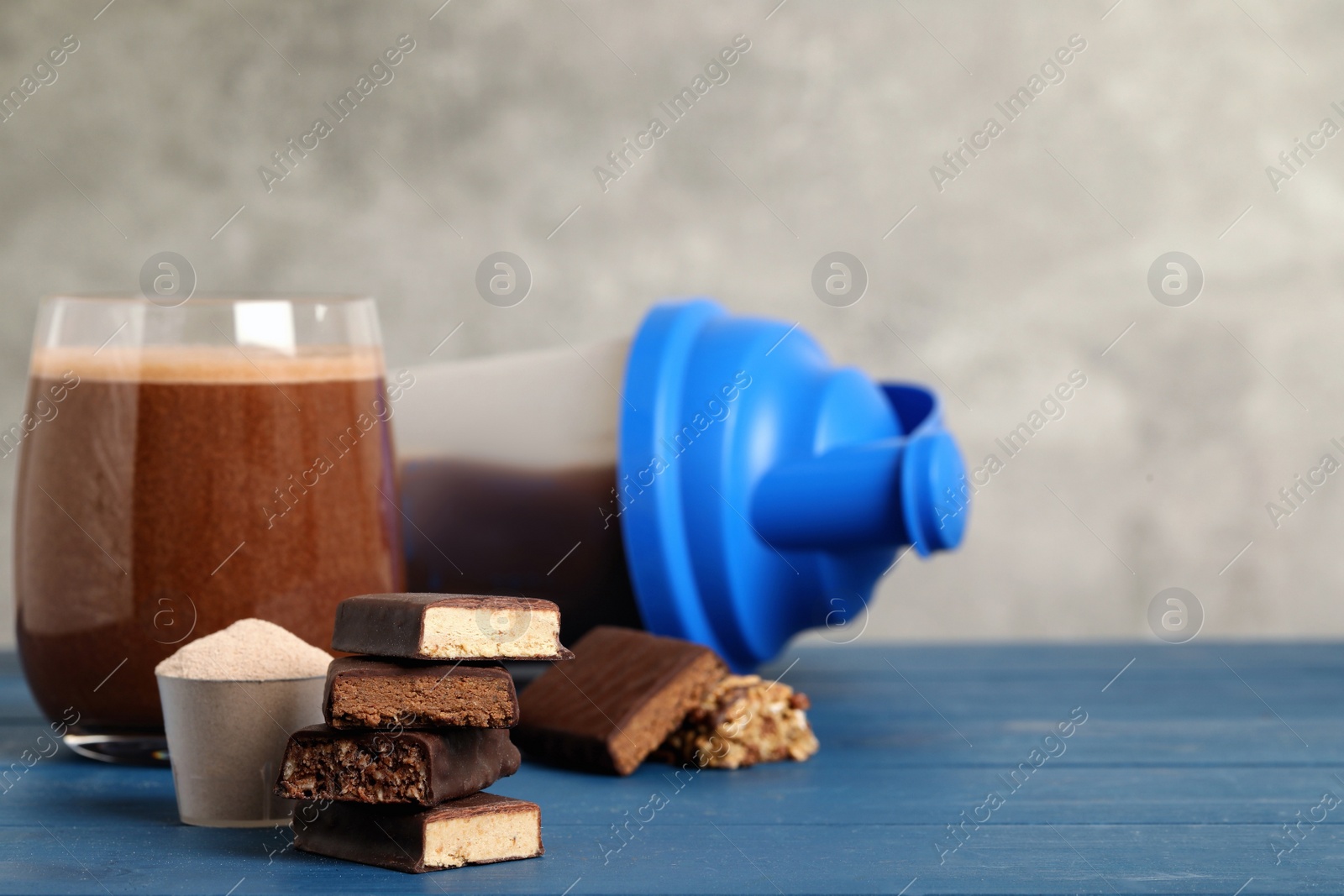 Photo of Different energy bars, protein cocktail and powder on blue wooden table. Space for text