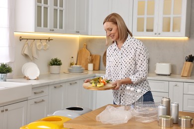 Photo of Smiling woman separating garbage at table in kitchen. Space for text