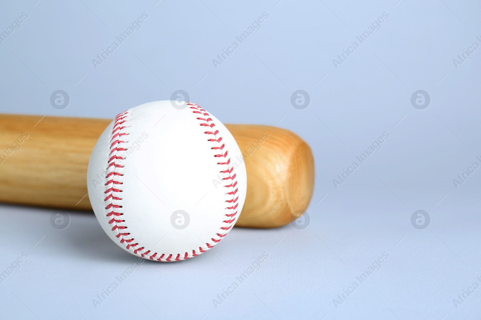 Photo of Wooden baseball bat and ball on light grey background, space for text. Sports equipment