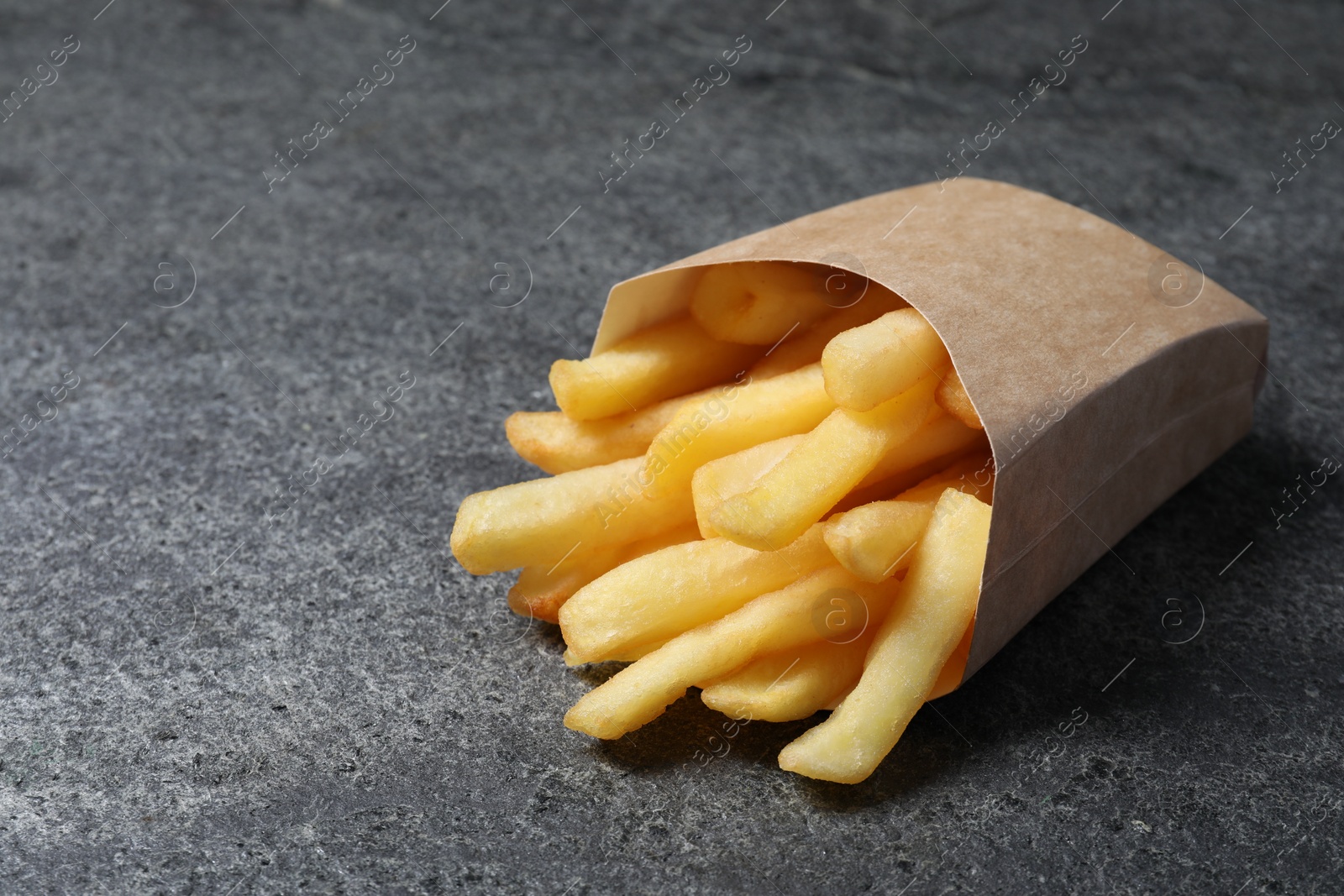 Photo of Delicious french fries in paper box on grey table, closeup. Space for text