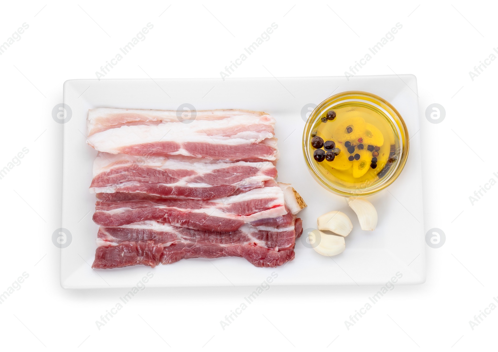 Photo of Pieces of raw pork belly, oil and garlic isolated on white, top view