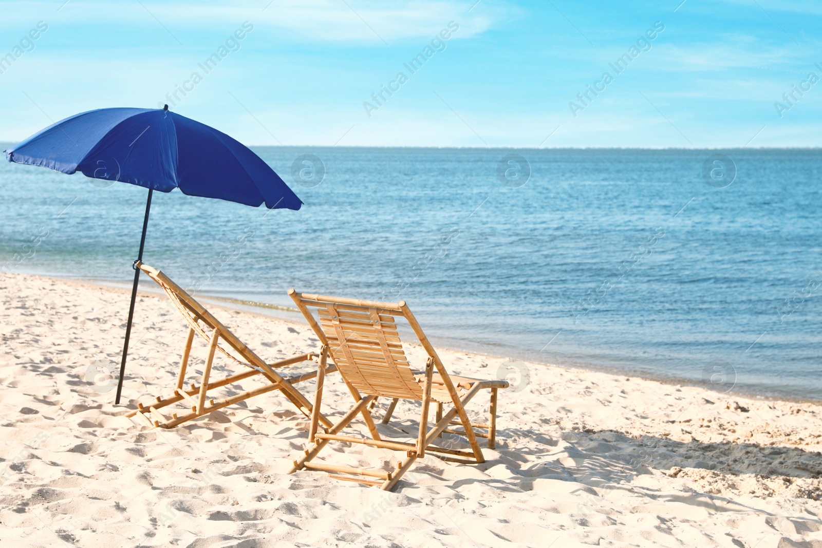 Photo of Empty wooden sunbeds and umbrella on sandy shore. Beach accessories