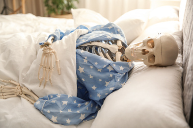 Photo of Human skeleton in pajamas lying on bed indoors