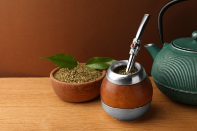 Calabash with mate tea, bombilla and teapot on wooden table