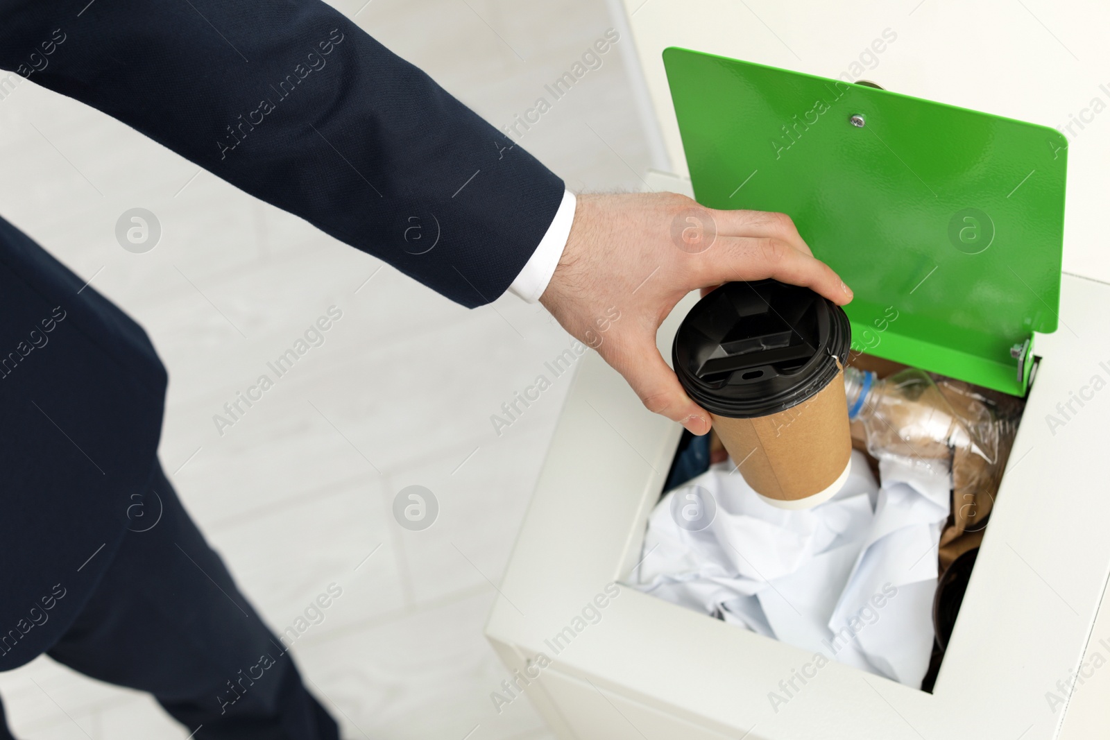 Photo of Man putting used paper cup into trash bin in office, closeup. Waste recycling