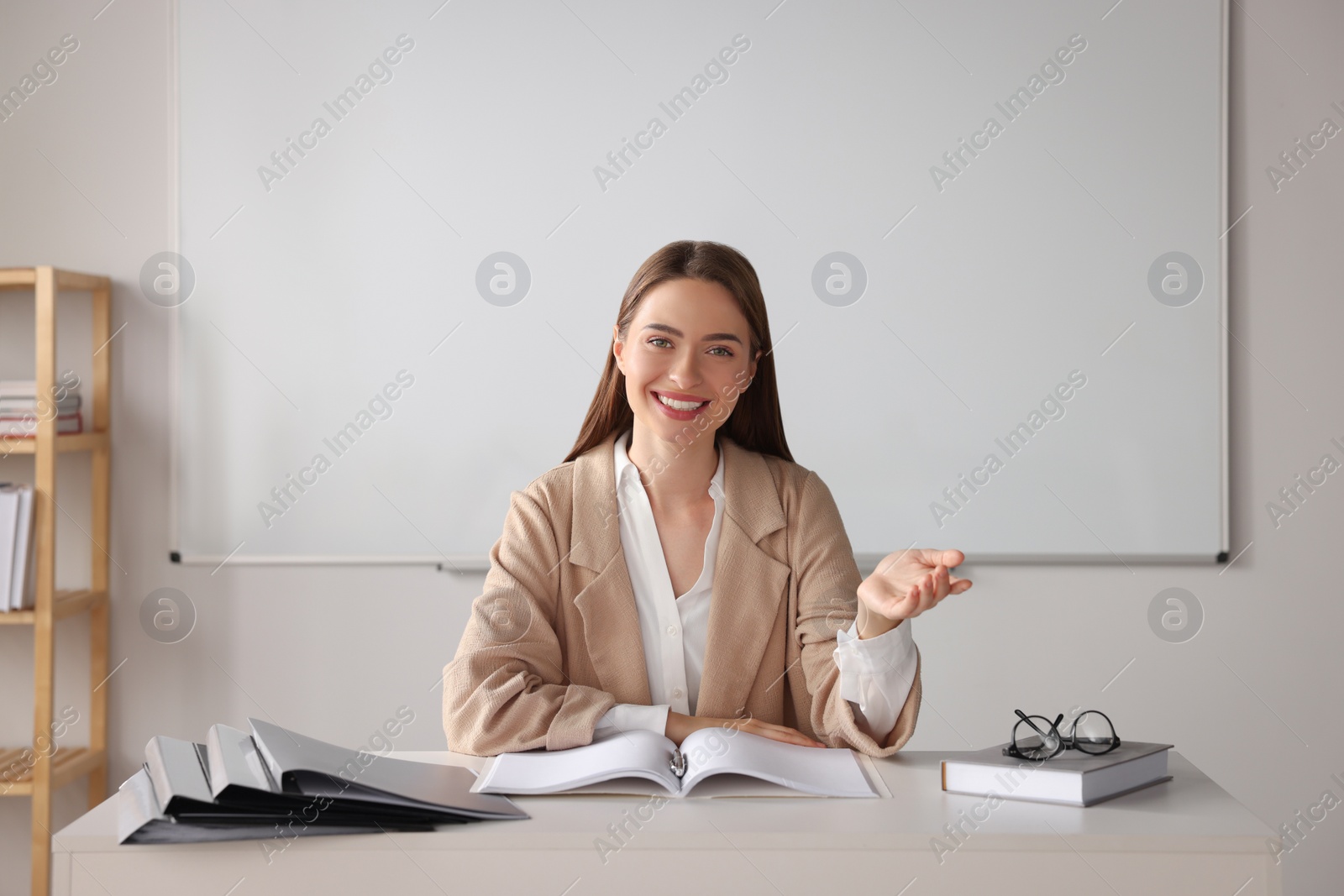 Photo of Happy young teacher explaining something at table in classroom