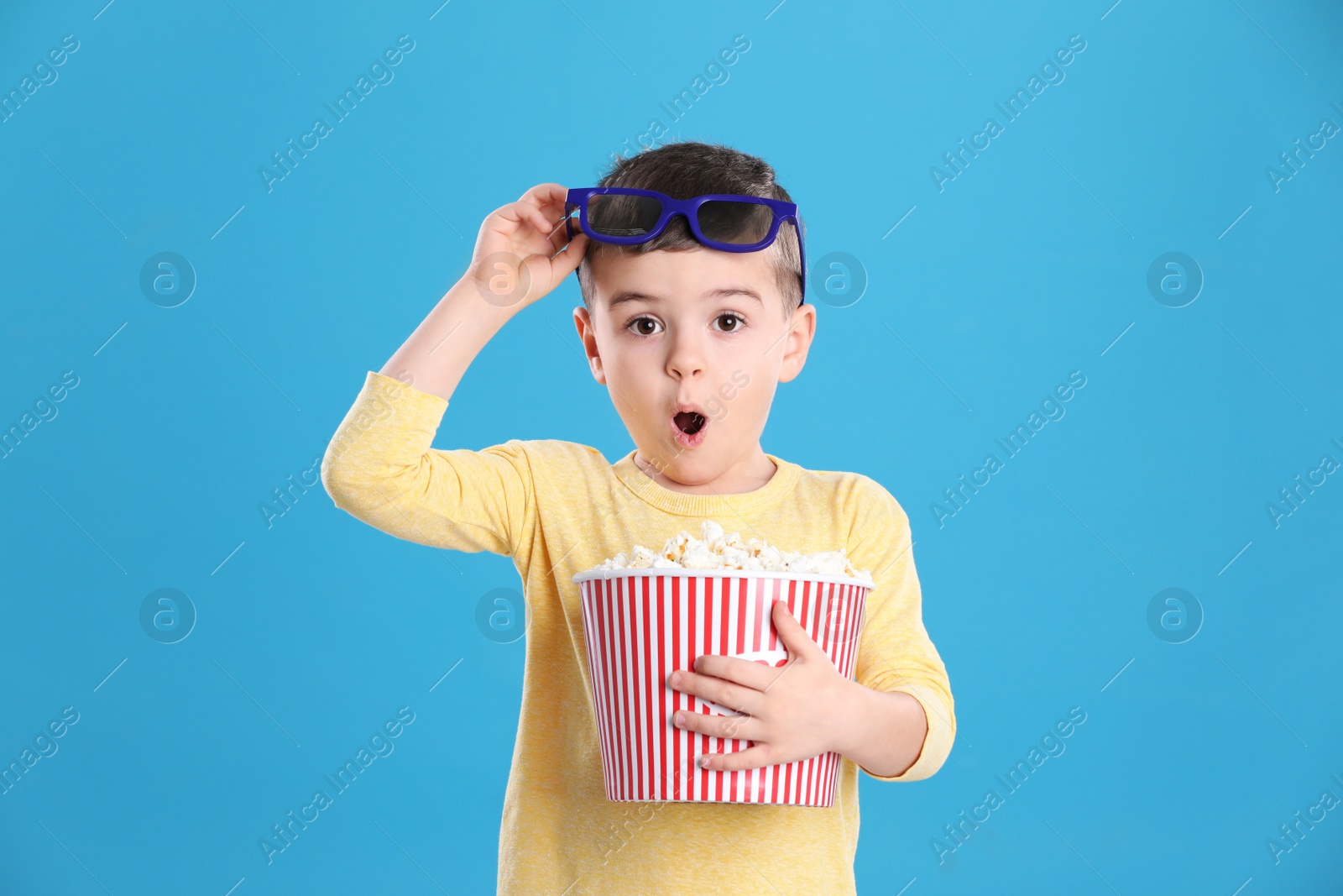 Photo of Cute little boy with popcorn and glasses on color background