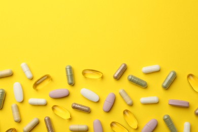 Different vitamin pills on yellow background, flat lay. Space for text