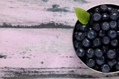 Photo of Ripe bilberries and leaf in bowl on wooden rustic table, top view. Space for text