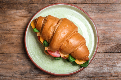 Photo of Tasty croissant sandwich on wooden table, top view
