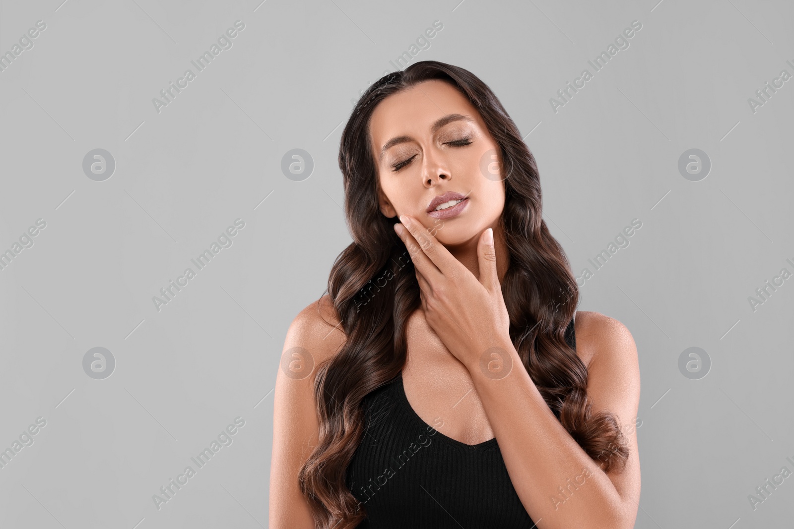 Photo of Hair styling. Beautiful woman with wavy long hair on grey background