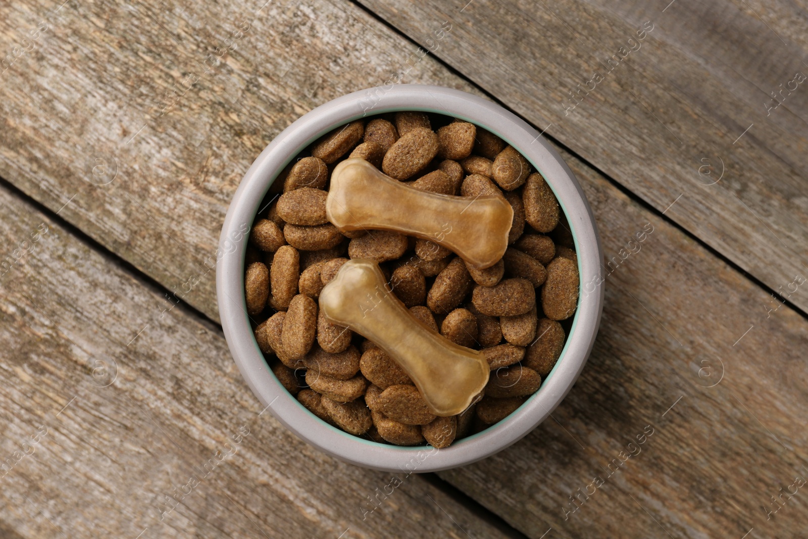 Photo of Dry dog food and treats (chew bones) on wooden floor, top view