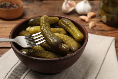 Photo of Fork with pickled cucumber over bowl on table, closeup