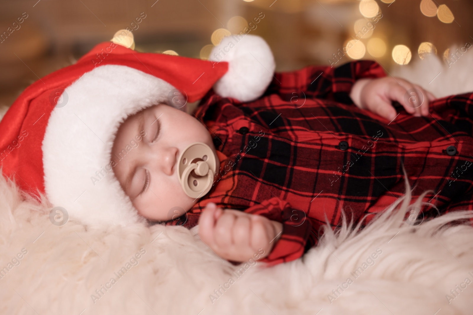 Photo of Cute baby in Santa hat sleeping on soft faux fur indoors. Christmas season