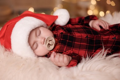 Cute baby in Santa hat sleeping on soft faux fur indoors. Christmas season
