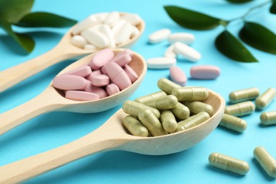 Photo of Different vitamin pills in spoons on light blue background, closeup