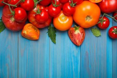 Photo of Many different ripe tomatoes on light blue wooden table, flat lay. Space for text