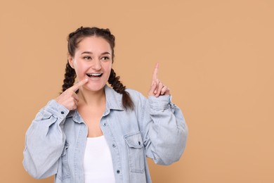 Photo of Smiling woman with braces pointing at something on beige background. Space for text