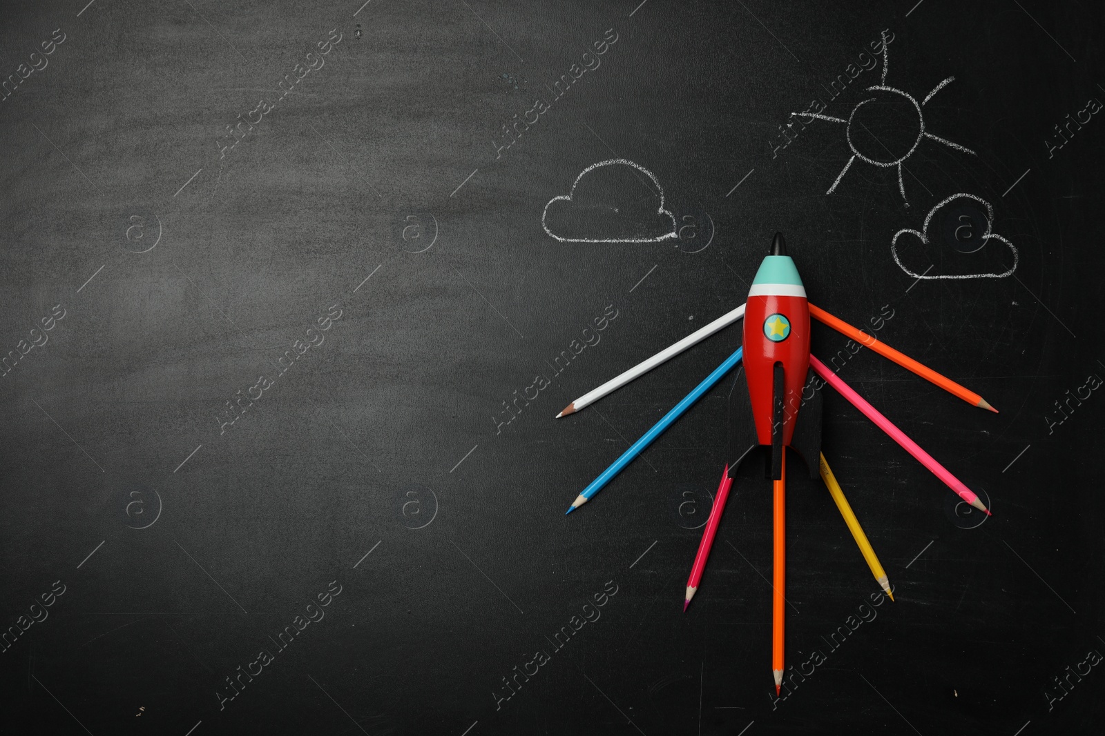 Photo of Bright toy rocket, school supplies and drawings on chalkboard, flat lay. Space for text