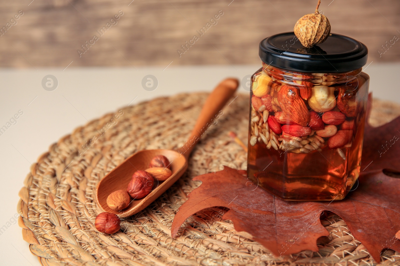 Photo of Different nuts with honey in jar, spoon and dry leaf on table, closeup. Space for text