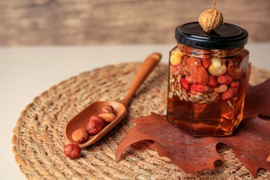 Photo of Different nuts with honey in jar, spoon and dry leaf on table, closeup. Space for text