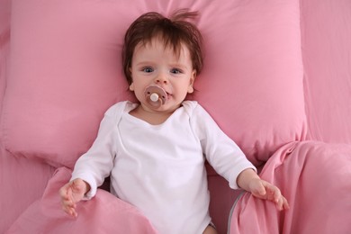 Cute little baby with pacifier on bed, top view