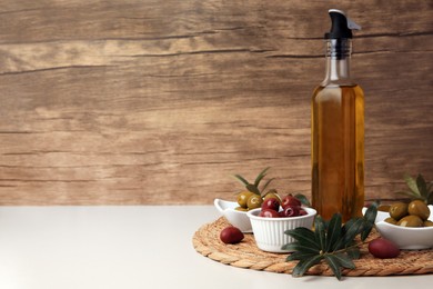 Photo of Bottle of oil, olives and tree twigs on beige table, space for text