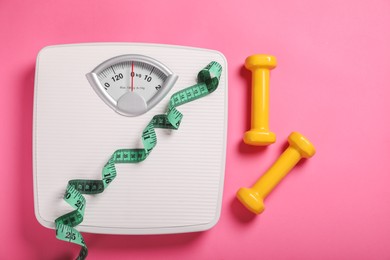 Photo of Weight loss concept. Scales, dumbbells and measuring tape on pink background, flat lay