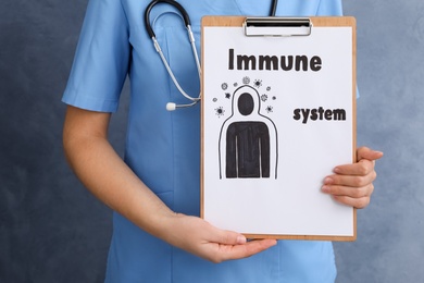 Woman holding clipboard with phrase Immune System on blue background, closeup