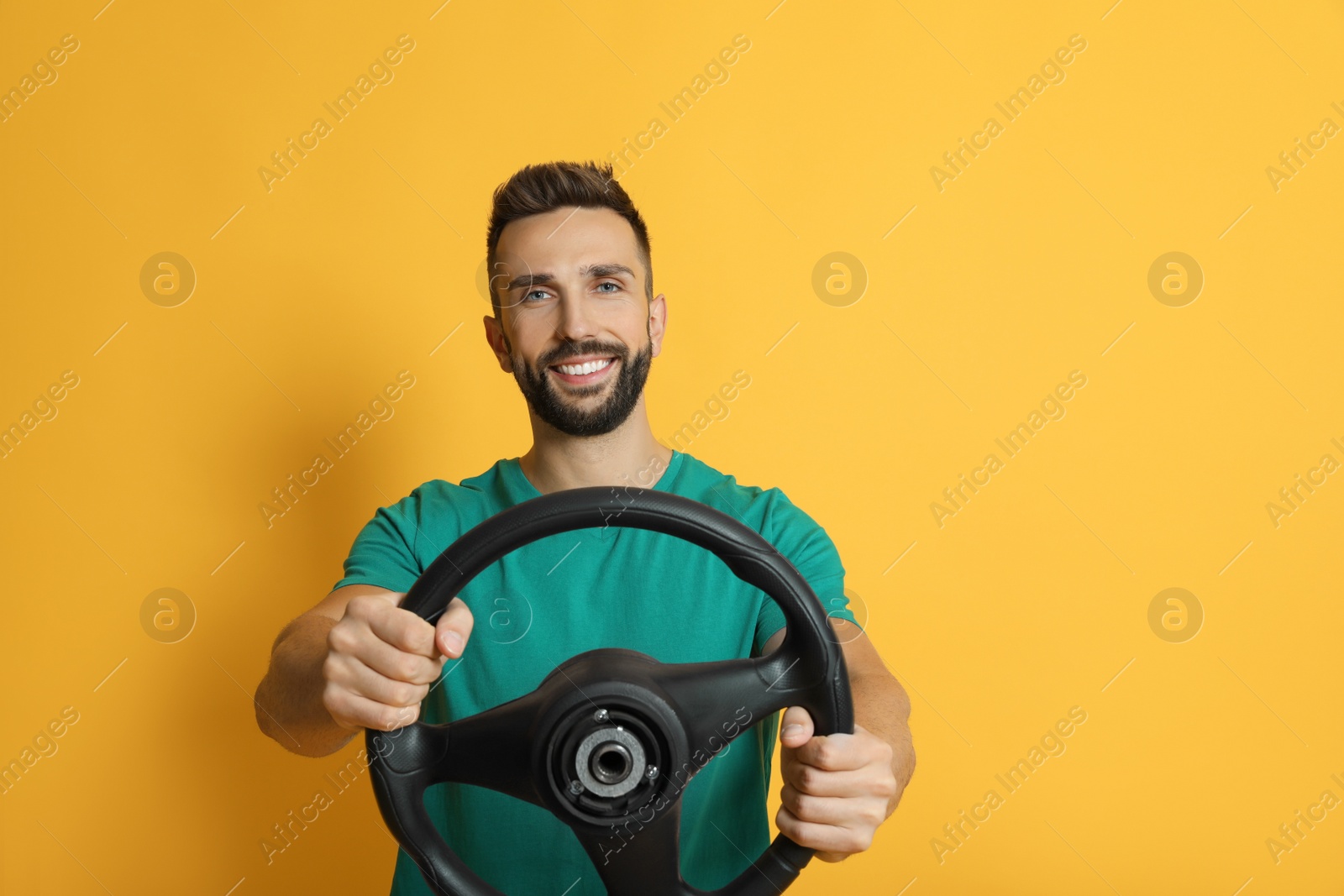 Photo of Happy man with steering wheel on yellow background