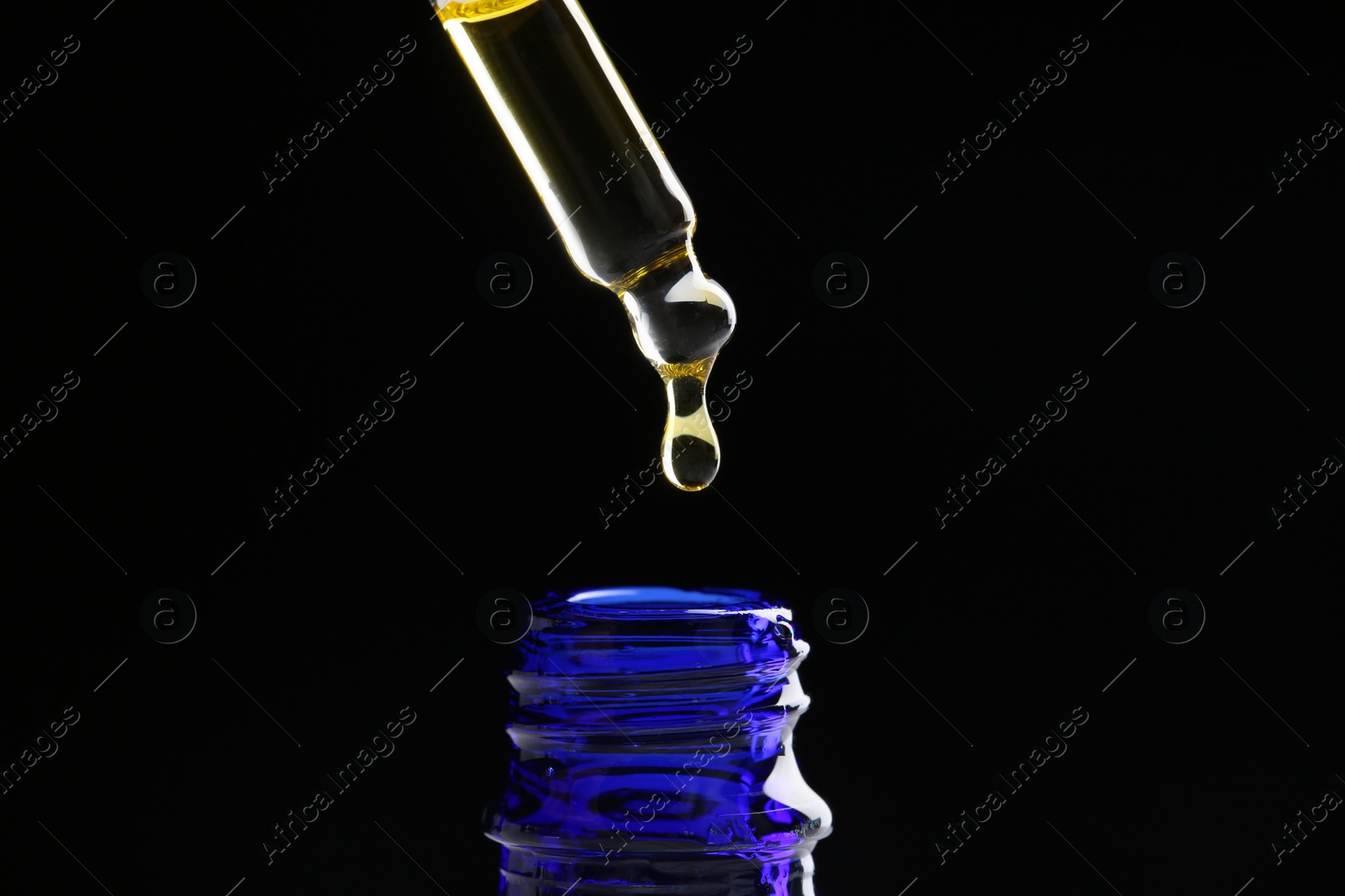 Photo of Dripping tincture from pipette into bottle on black background, closeup