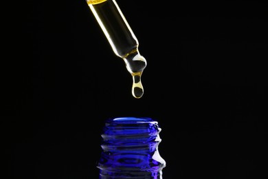 Photo of Dripping tincture from pipette into bottle on black background, closeup