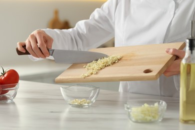 Photo of Professional chef putting cut garlic into bowl at white marble table indoors, closeup