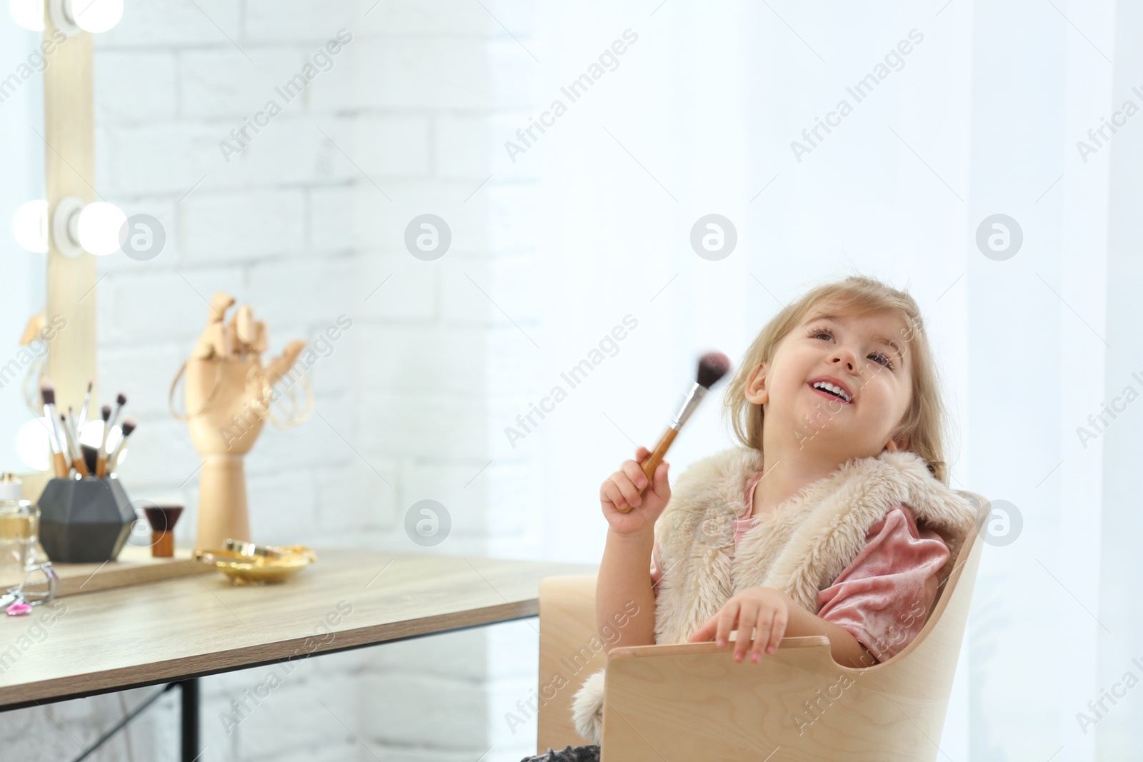 Photo of Cute little girl playing with cosmetics in dressing room