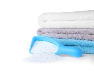 Laundry detergent in plastic measuring scoop and towels on white background