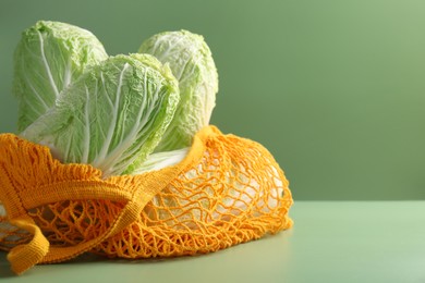 Photo of Fresh Chinese cabbages in string bag on green background, closeup. Space for text