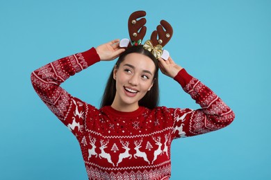 Photo of Young woman in Christmas sweater and reindeer headband on light blue background