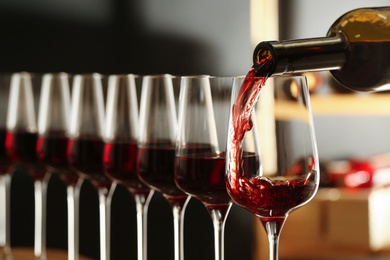 Pouring wine from bottle into glass in cellar, closeup