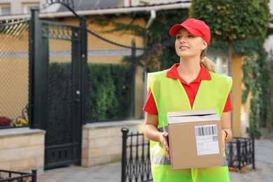 Courier in uniform with parcel near private house outdoors, space for text