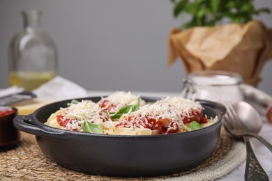 Photo of Delicious pasta with tomato sauce, basil and parmesan cheese on wicker mat