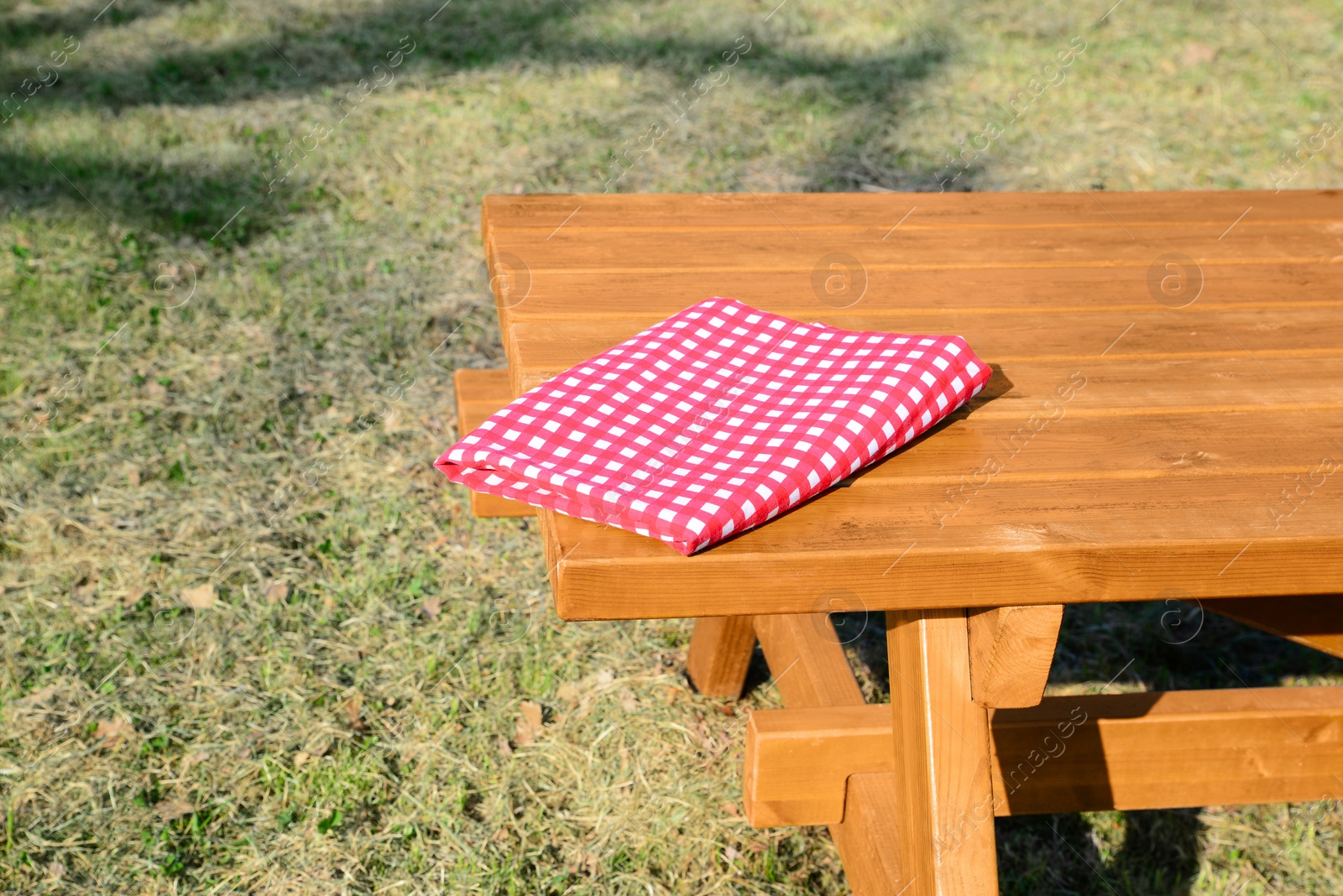 Photo of Folded red and white checkered tablecloth on wooden picnic table in park