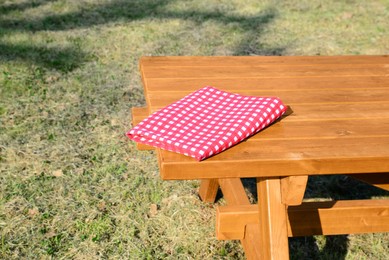 Photo of Folded red and white checkered tablecloth on wooden picnic table in park