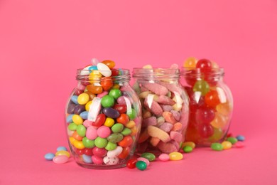 Photo of Glass jars with lots of different candies on bright pink background