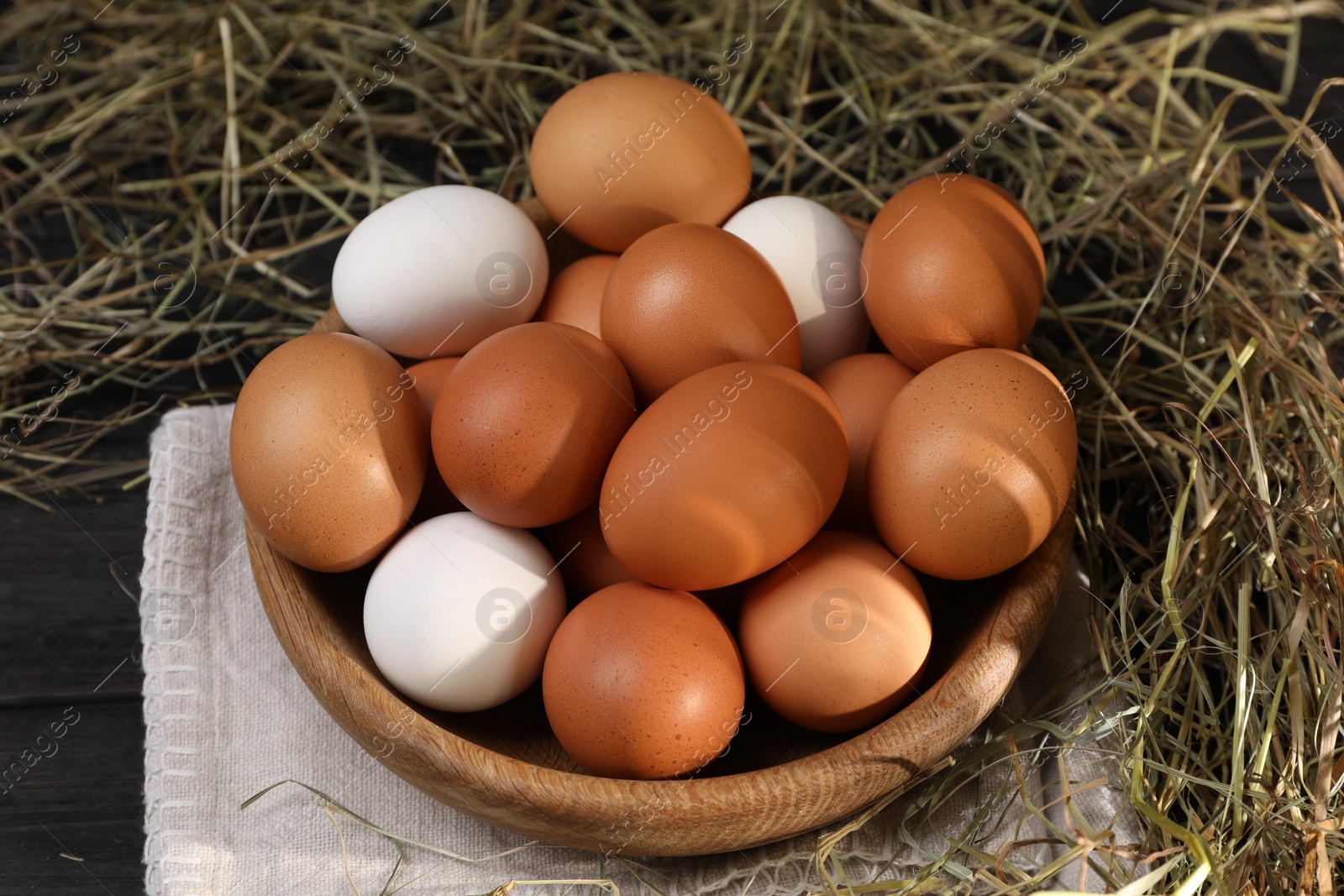 Photo of Fresh chicken eggs in bowl and dried hay on black wooden table