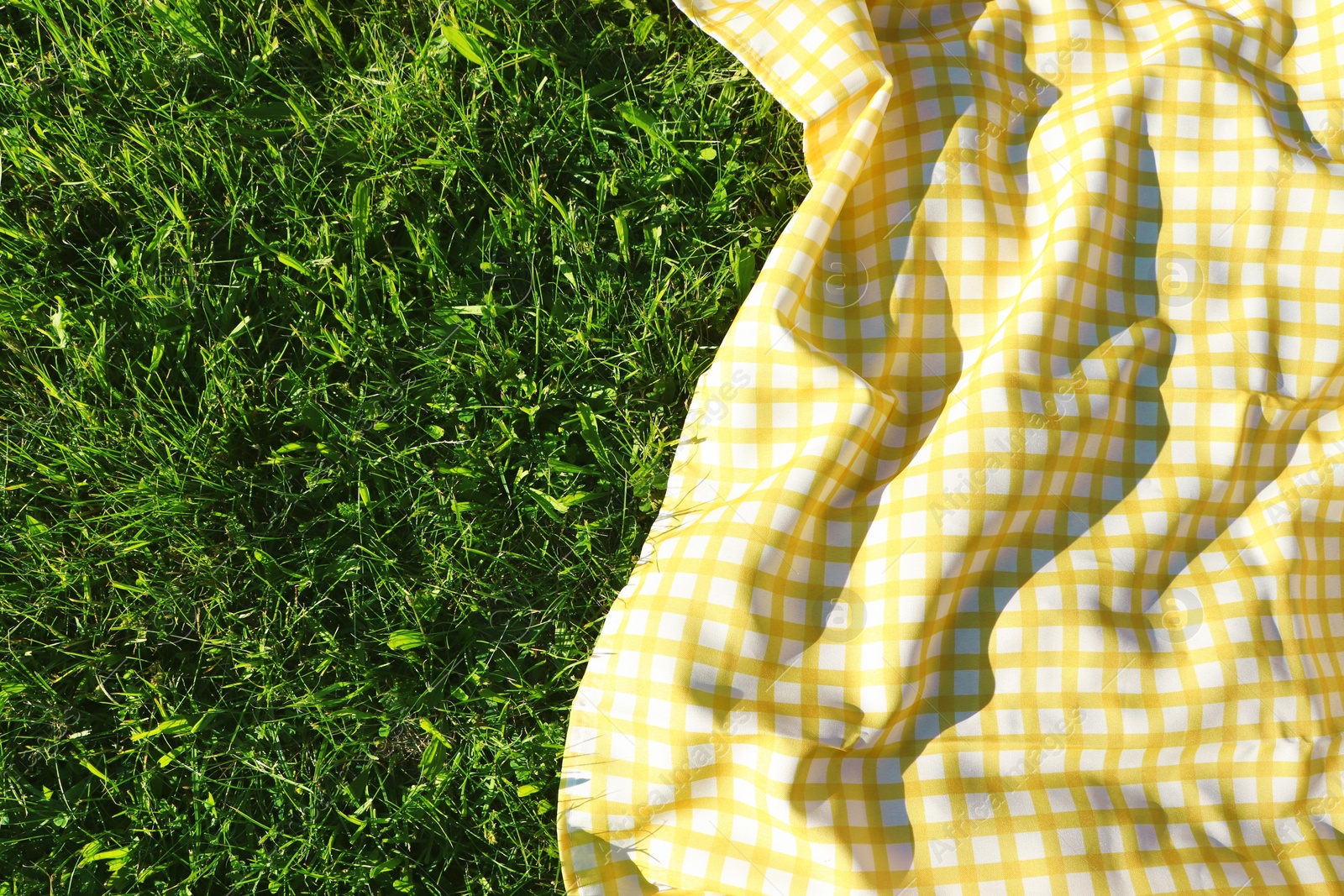 Photo of Checkered picnic tablecloth on fresh green grass, top view. Space for text