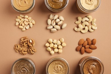 Many tasty nut butters in jars and nuts on beige table, flat lay